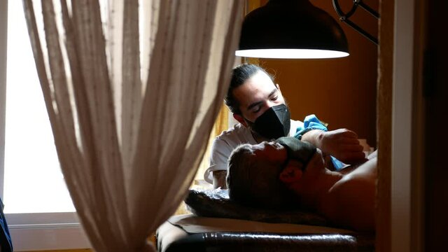 View through curtains of a tattoo artist working with a client.