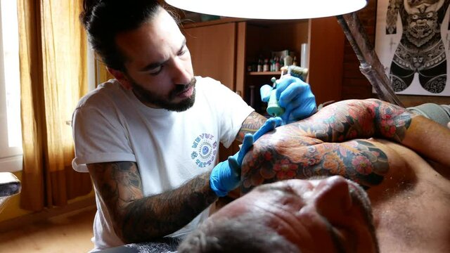 Side view of tattoo artist working on a customer's arm in his studio.
