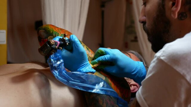 Side view of tattoo artist working on a customer's arm in his studio.