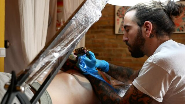 Side view of tattoo artist working on a customer's arm in his studio.