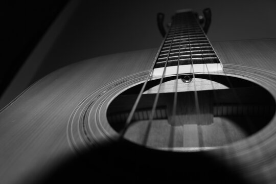 A perspective over the inside of an Acoustic Guitar aiming the truss rod. The 6 strings make their path from bottom up in a classic interation of wood and steel that characterize this instrument