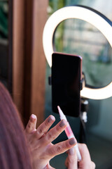 unrecognizable woman showing makeup in front of a tripod with circular light and her cell phone. female influencer blogger live in front of her smartphone. social media concept
