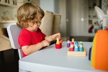 Little boy playing with wooden toy figures at the table