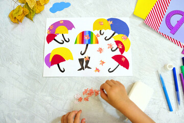 Autumnal application of still life. Child cutting from paper multicolor umbrellas, crafts for kids.