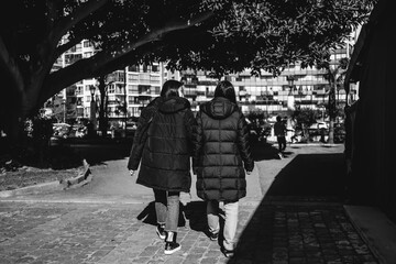 Two women walking through a park in the city in the day (in black and white)