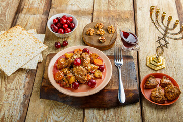 Jewish dish stewed potatoes with chicken in cherry sauce, decorated with cherries on a stand next to matzo and menorah.