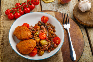 Cod cutlets with potatoes and vegetables on a round stand next to the ingredients.