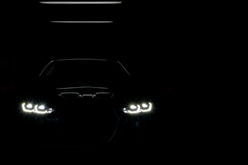 Unclear shape of front view sport car with headlights on dark background, Concept car concept,...