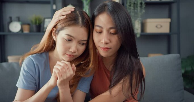 Asian women teenager embracing to calm her sad best friends from feeling down from breakup with boyfriend in living room at home. Friendship counseling and care, unhappy girl support her girlfriend.