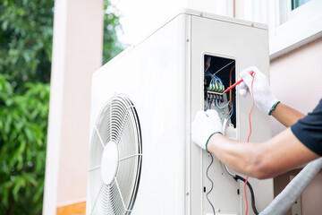 Technician using measuring equipment checking electric at circuit breaker on outdoor air compressor...