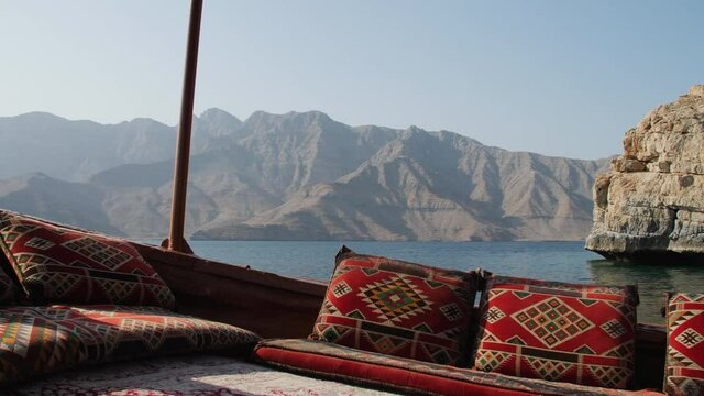 Tracking shot of ocean and fjords from the POV of a traditional Dhow boat moving through the water with colorful geometric pillows on a clear sunny day in Khasab, Musandam Oman.