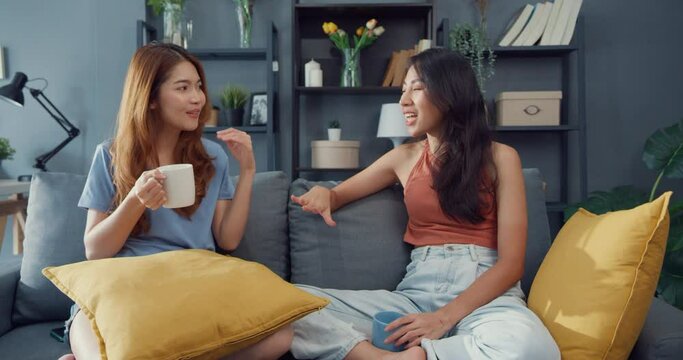 Asia housewife women with casual relax on couch with cup of tea talk together about their life and husband relationship gossip in living room at house. Girls friends roommate stay in dorm together.