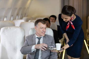 flight attendant serving water and cup of tea or coffee to businessman passenger in airplane