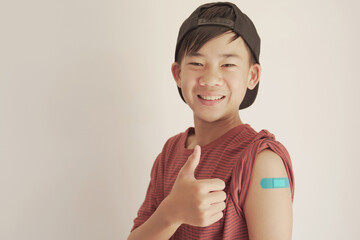 Mixed Asian teen boy giving thumb up and showing his arm with blue bandage after got vaccinated or ...