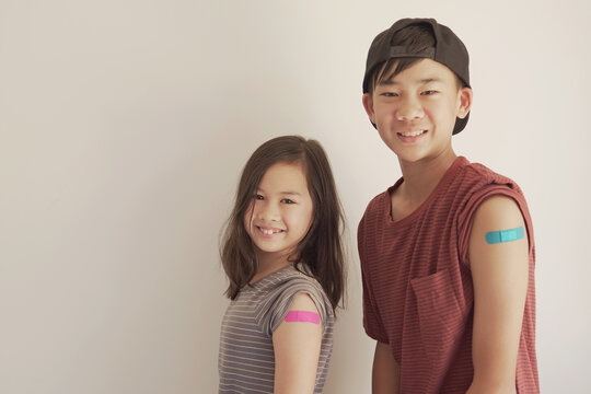 Mixed Asian young girl and teen boy showing their arms with blue bandage after got vaccinated or  inoculation, child immunization, covid delta vaccine concept