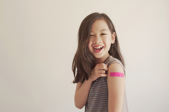 Mixed Asian young girl showing her arm with pink bandage after got vaccinated or  inoculation, child immunization, covid omicron vaccine concept
