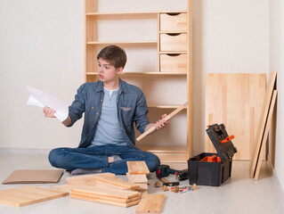 Young  man assembling furniture at home. Puzzled teenager trying to read the diy instruction with...