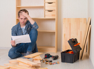 Young  man assembling furniture at home. Teenager trying to read the diy instruction with problems...