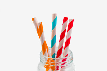 Collection of coloured paper straws in a glass jar against on white background.