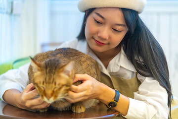 Young Asian woman sitting on floor playing and stroking adorable cat with happiness. Pretty girl enjoy indoor lifestyle with friendly cat at home. Pet and owner friendship and relationship concept