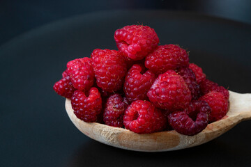 Wooden spoon full of raspberries isolated on black background