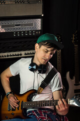 Handsome young man in green baseball cap and white t-shirt with electric guitar in recording studio. Rock musician performance. Rehearsal base. Rock music concept. Atmosphere on background.