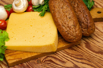 a piece of cheese greens lettuce cherry tomatoes mushrooms and rye buns on a wooden cutting board on the table