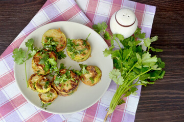 Grilled zucchini lie on a light plate, which stands on a towel, spread out on a dark background of the table