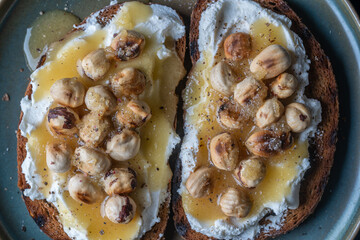Two bread toast with cream cheese, roasted hazelnuts, honey, pepper and salt, close up, top view