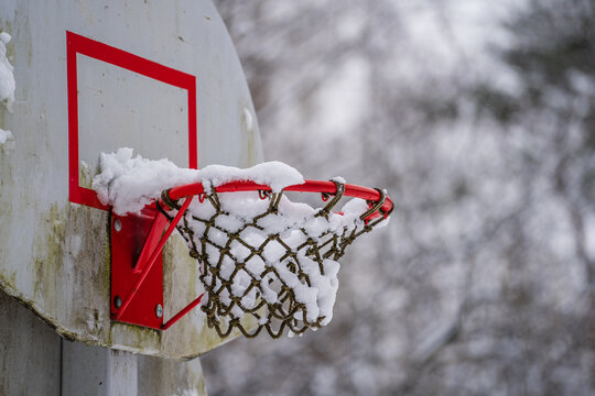Basketball hoop net after snowstorm filled with snow in winter park, Ukraine. Winter basketball backboard