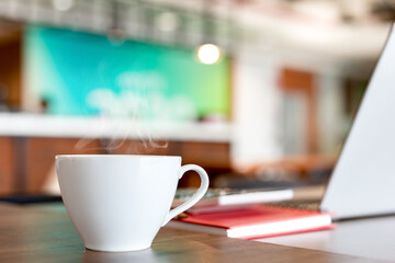 Blurred of cup of hot coffee on wooden table with computer