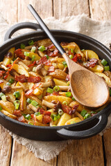 Fried potatoes with bacon and honey fungus mushrooms close-up in a frying pan on the wood background. Vertical