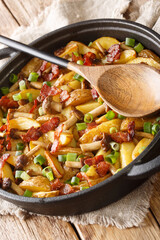 Fried potatoes with bacon and mushrooms close-up in a frying pan on the table. Vertical
