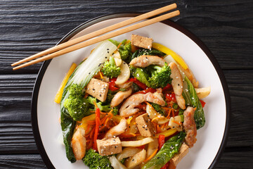 Tasty Stir fry mix of vegetables, chicken and tofu close-up in a plate on the table. Horizontal top view from above