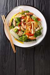 Asian Stir fry pepper,  pak choi, carrots, broccoli, chicken and tofu close-up in a plate on the table. Vertical top view from above