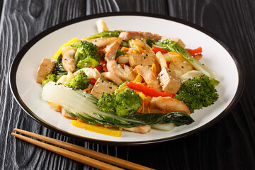 Stir Fried Asian mix of chicken, tofu and seasonal vegetables close-up in a plate on a black wooden background. horizontal