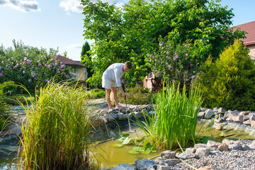 man cleans garden pond bottom with high-pressure washer from mud and sludge.