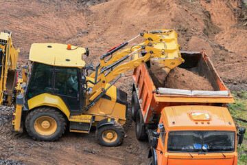  A miniature backhoe loader loads the soil into a dump truck.