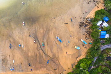 .aerial top view fishing boats parking on the beach during low tide at Rawai beach Phuket Thailand..sea without water in low tide fishing boats stuck in the mud...sand beach background..