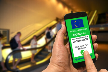 A man in a shopping mall holds a smartphone with the European Union digital green pass for Covid-19 in his hand. Safety concept for Coronavirus and the Green pass