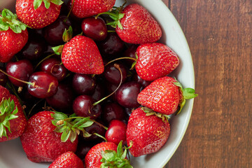 Strawberries and cherries in a white bowl on a wooden table.