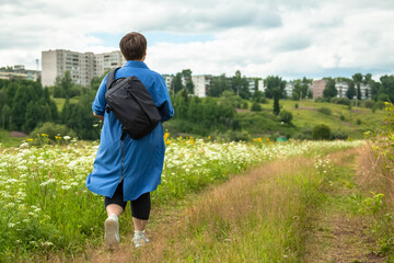 Grandmother is walking along a path in a field of flowers. An elderly woman walks in nature.