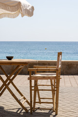 Parasol, wooden table and chair in a beach bar on a promenade by the sea