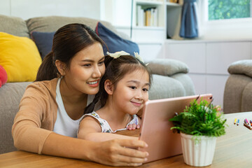 Asian mother and her daughter using tablet for study online together in liveing room.