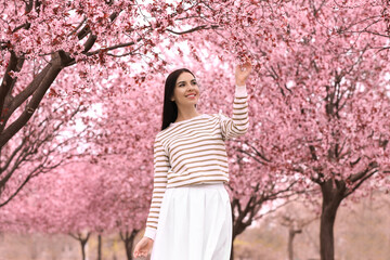 Pretty young woman in park with blooming trees. Spring look