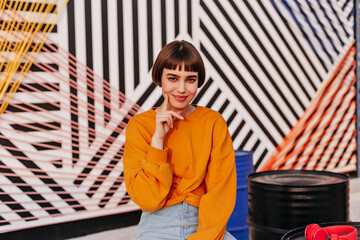 Charming woman with short hairstyle cute smiling on striped backdrop. Lovely girl in orange...