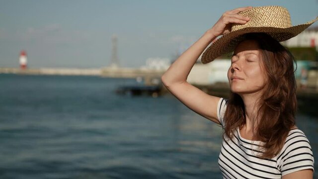 middle-aged woman on vacation by the sea enjoys the rays of the morning sun puts on a big hat