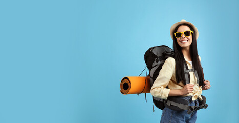 Obraz premium Happy female tourist with backpack on light blue background. Space for text