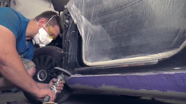 The master restores the retro car from rust corrosion. He repairs the thresholds and cleans them with a special sander or grinder. Old-school cars, a restoration workshop. The master with glasses.