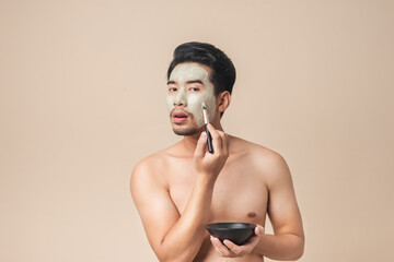 Portrait of Asian man applying clay mask on face for facial treatment and skin rejuvenation in...